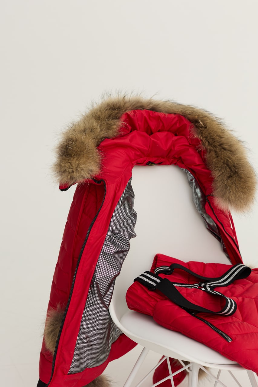 Red winter coat with fur hood on a white chair against a light background