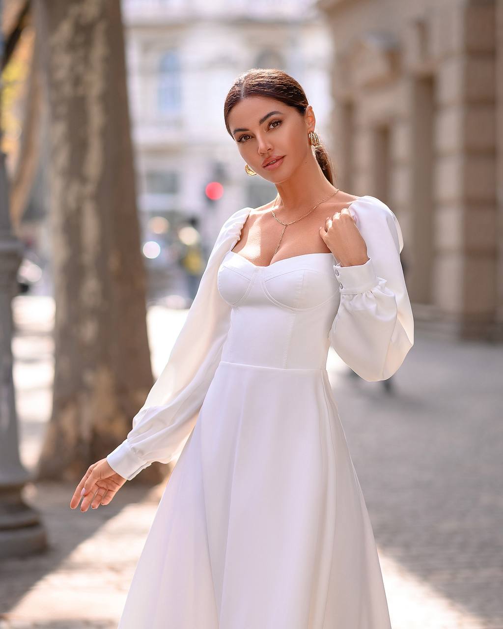 Woman in a white dress with a sheer cardigan standing on a street.