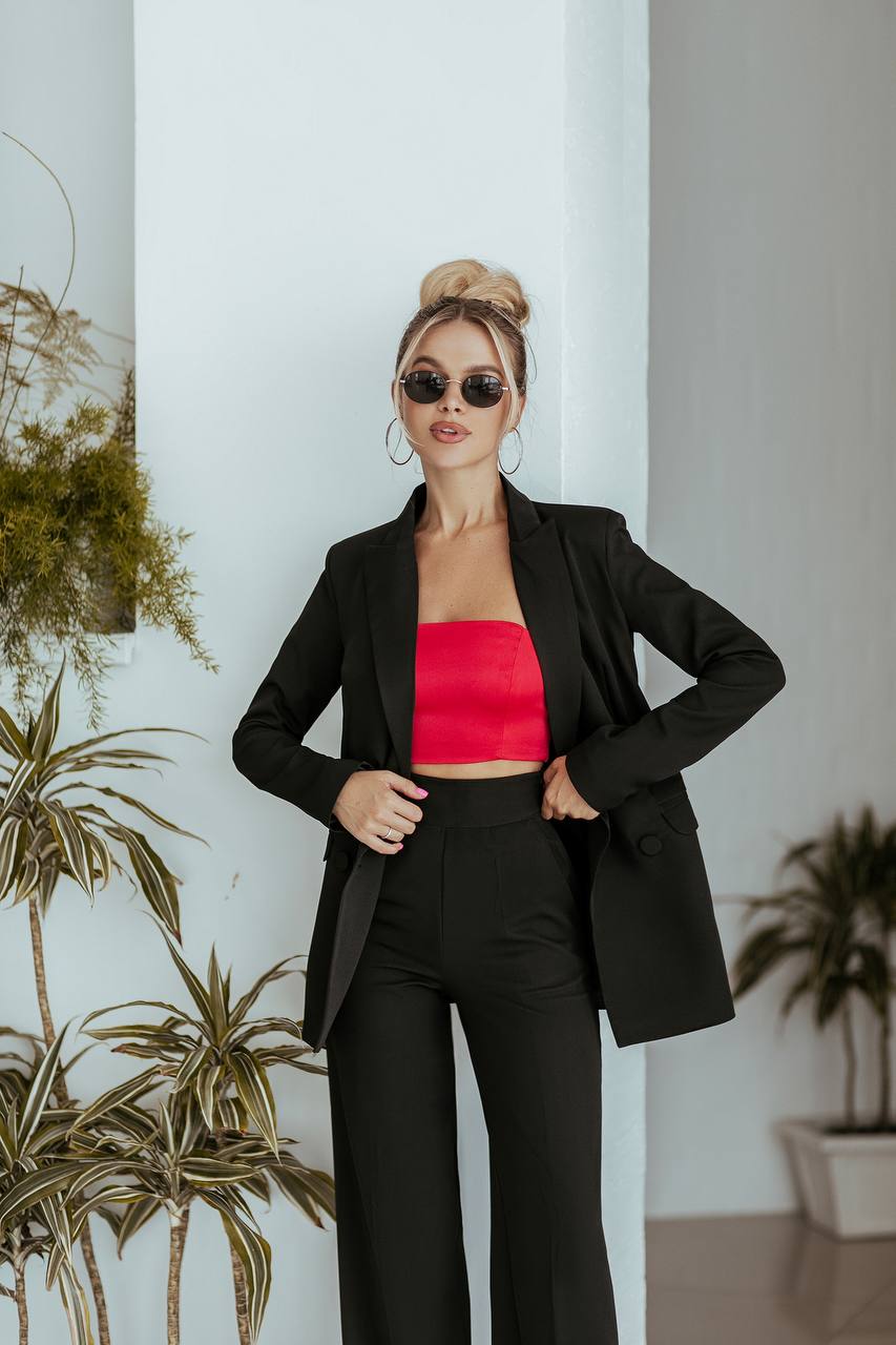 Woman in a black blazer and red top standing in a room with plants.