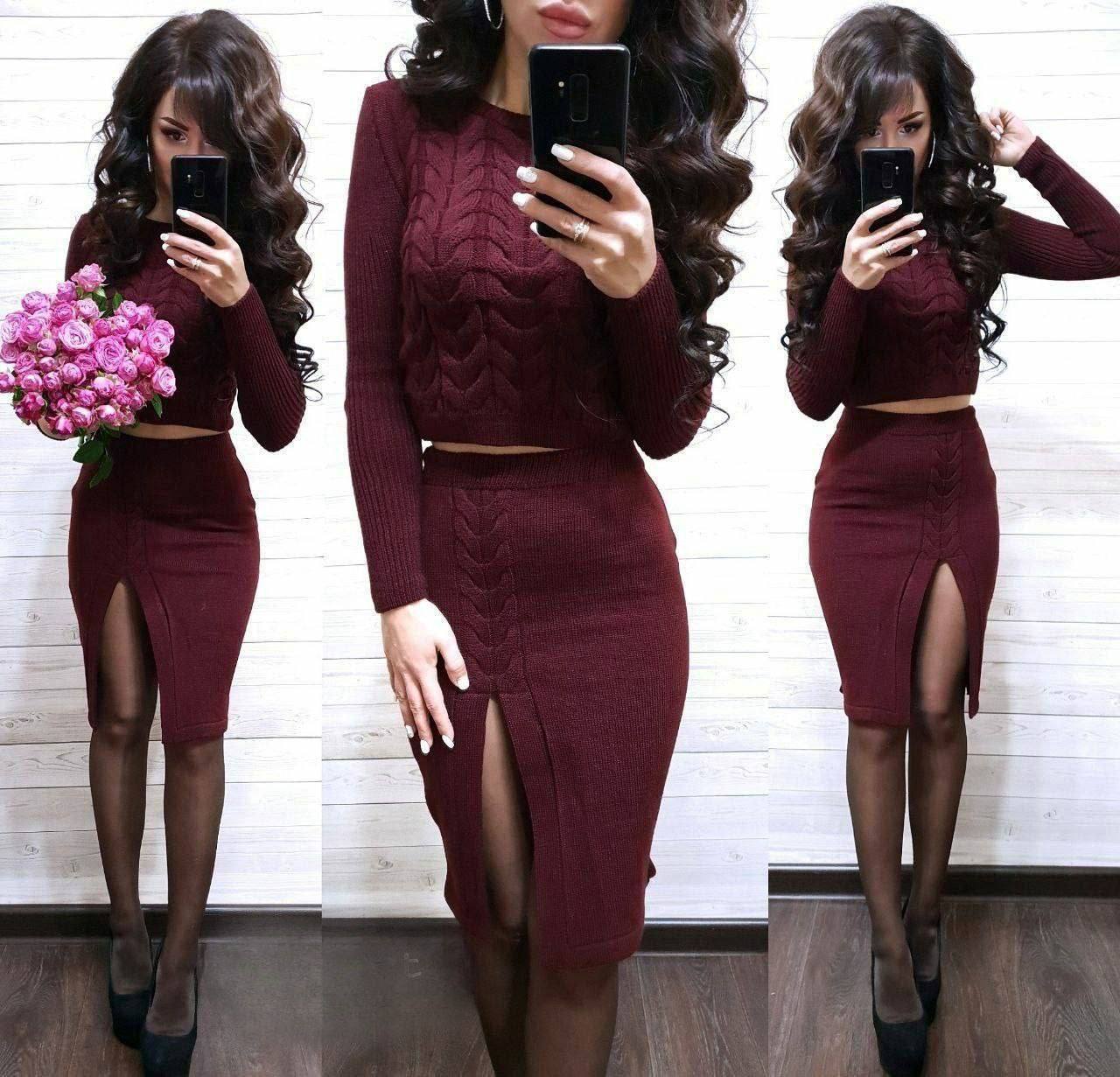 Woman in a burgundy two-piece outfit with a skirt and top, holding pink flowers.
