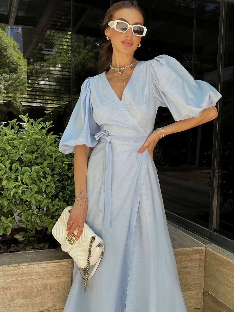 Woman in a light blue dress with puffed sleeves standing outdoors.