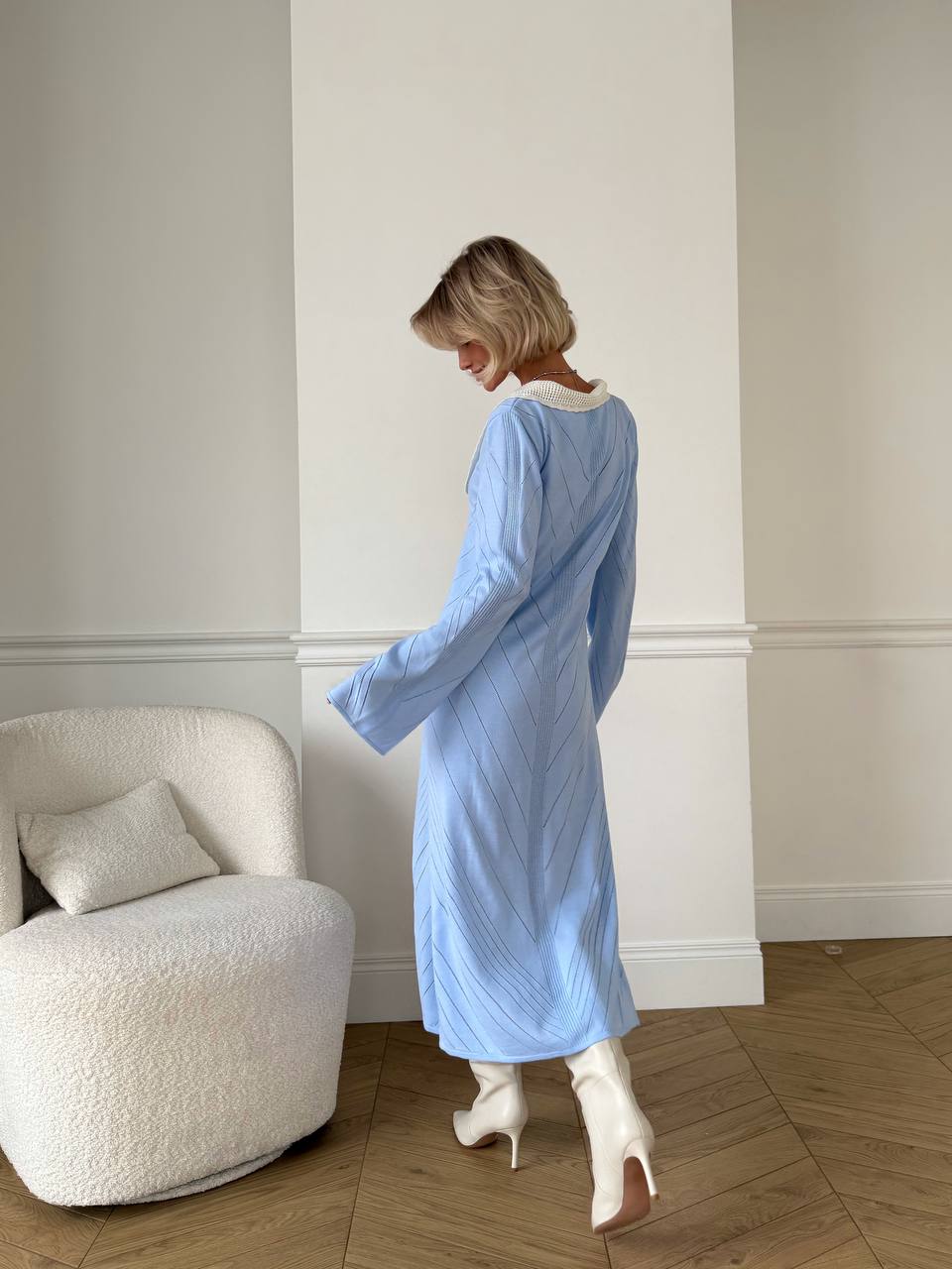 Woman in a light blue dress standing in a room with a white armchair.