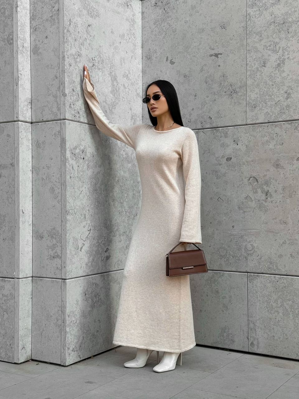 Woman in a long white dress standing against a gray concrete wall.