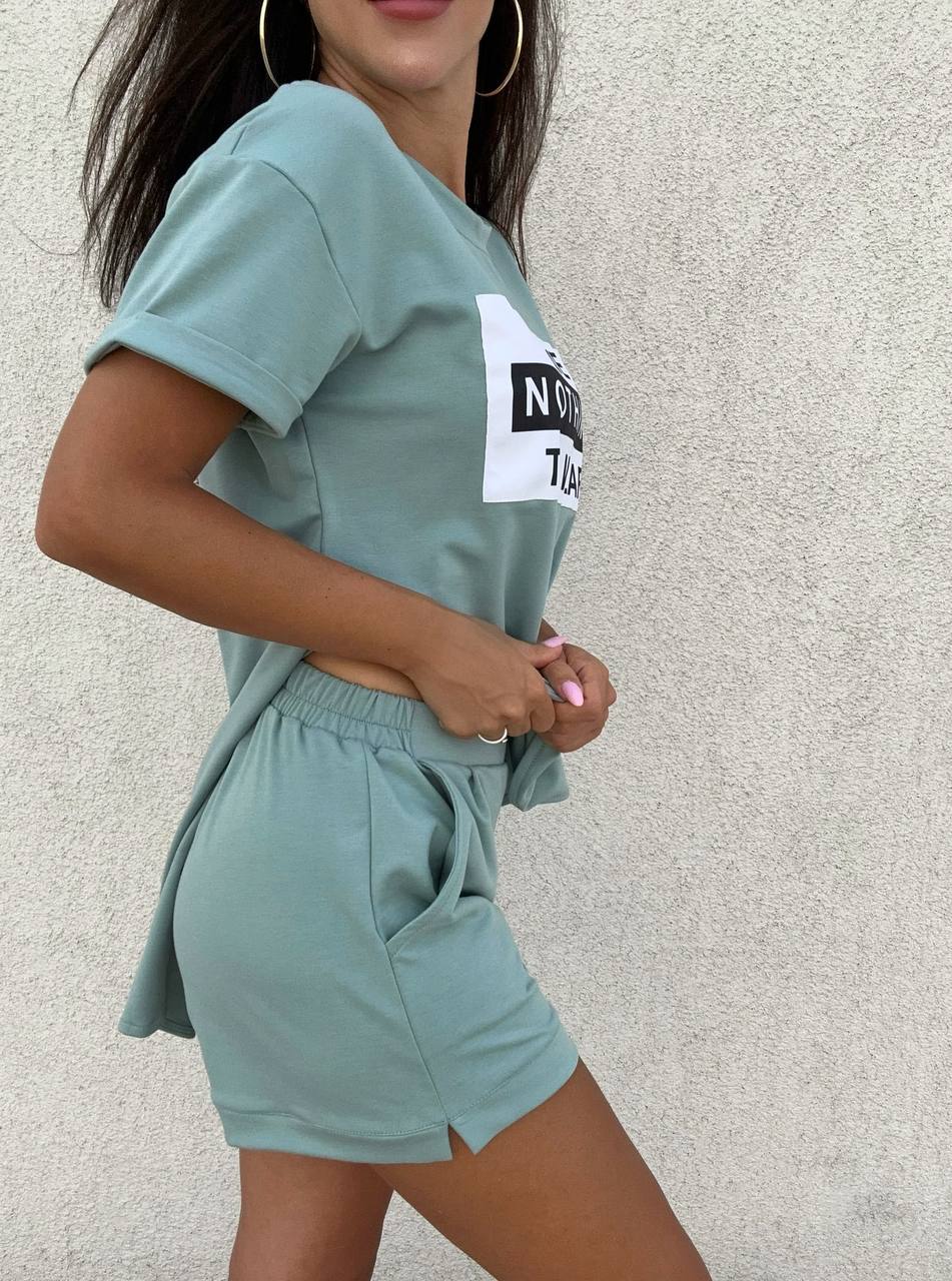 Person wearing a teal outfit with a logo on a light gray background