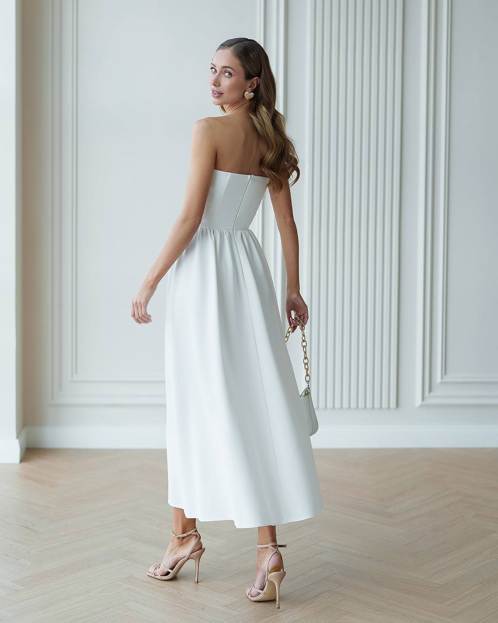 Woman in a strapless white dress standing in a room with white paneled walls.