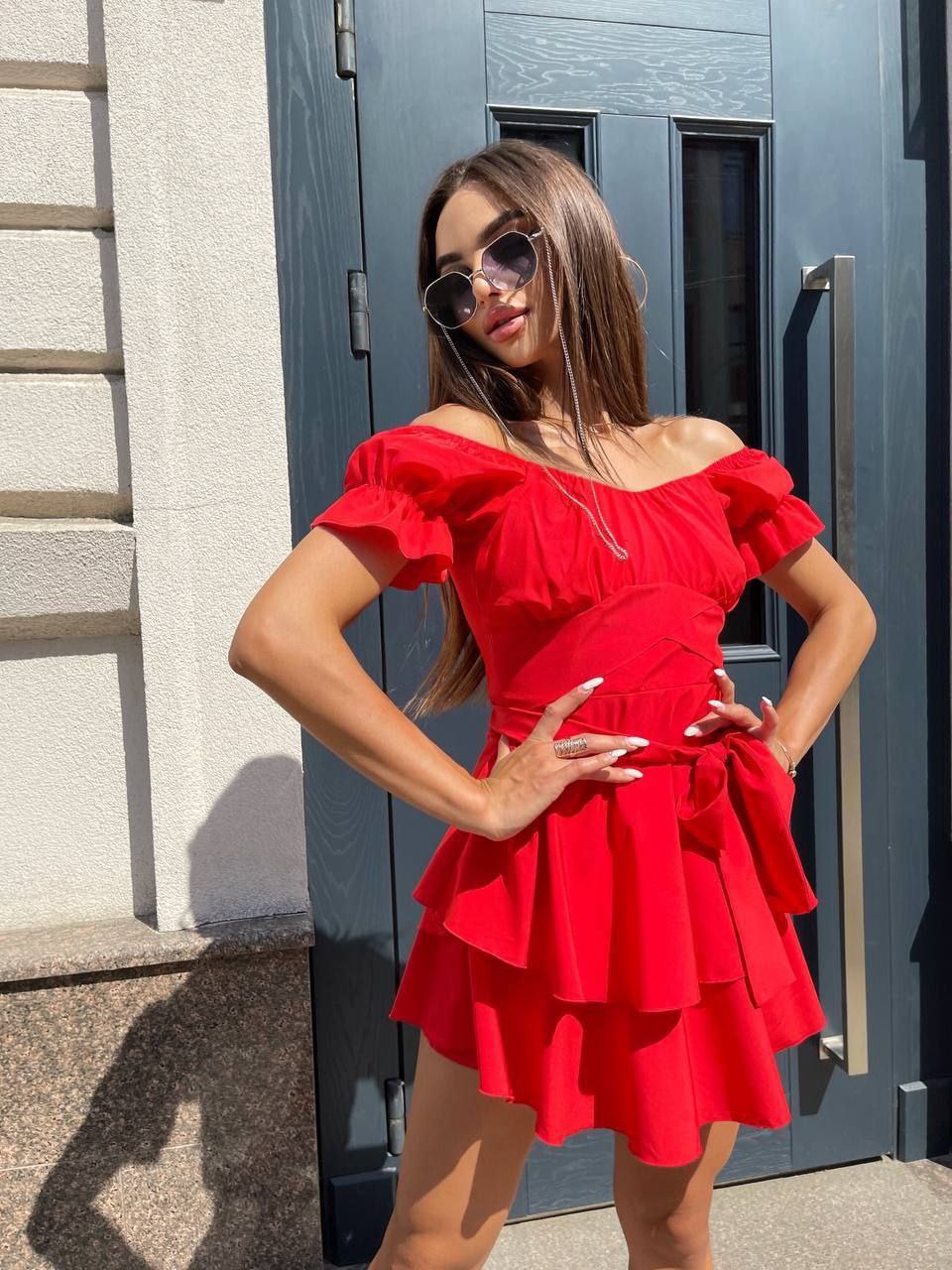 Woman wearing a red off-shoulder dress standing in front of a gray door.