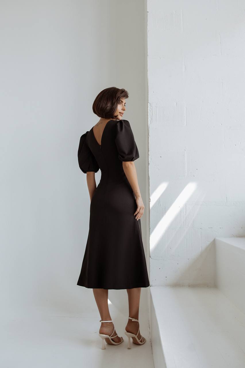 Woman in a black dress standing in a sunlit room with white walls.