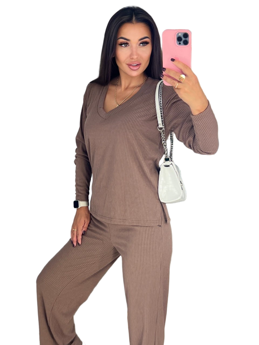 Woman taking a selfie wearing a brown ribbed outfit with a white handbag on a white background