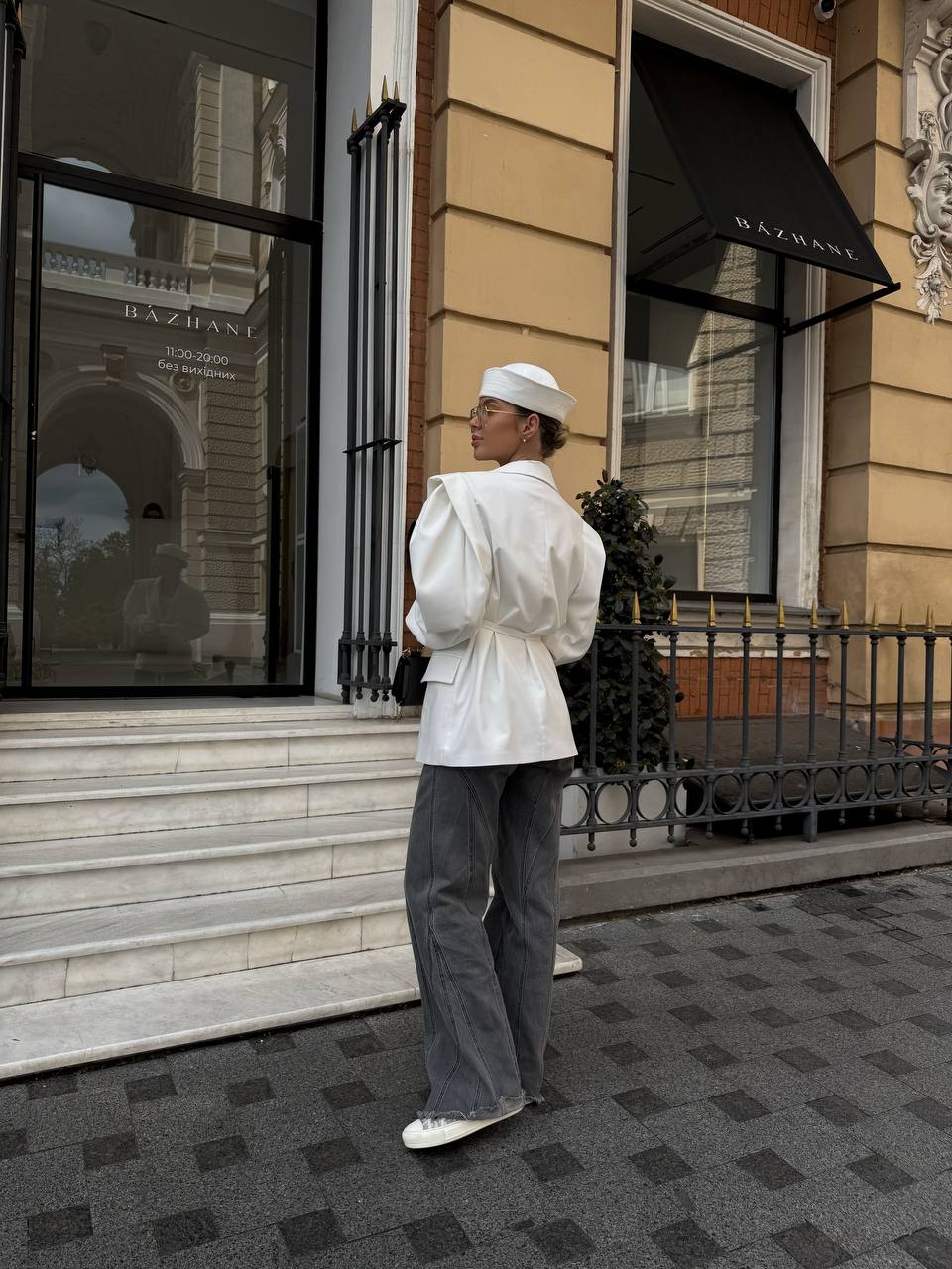 Person in white outfit and hat standing on steps in front of a building entrance.