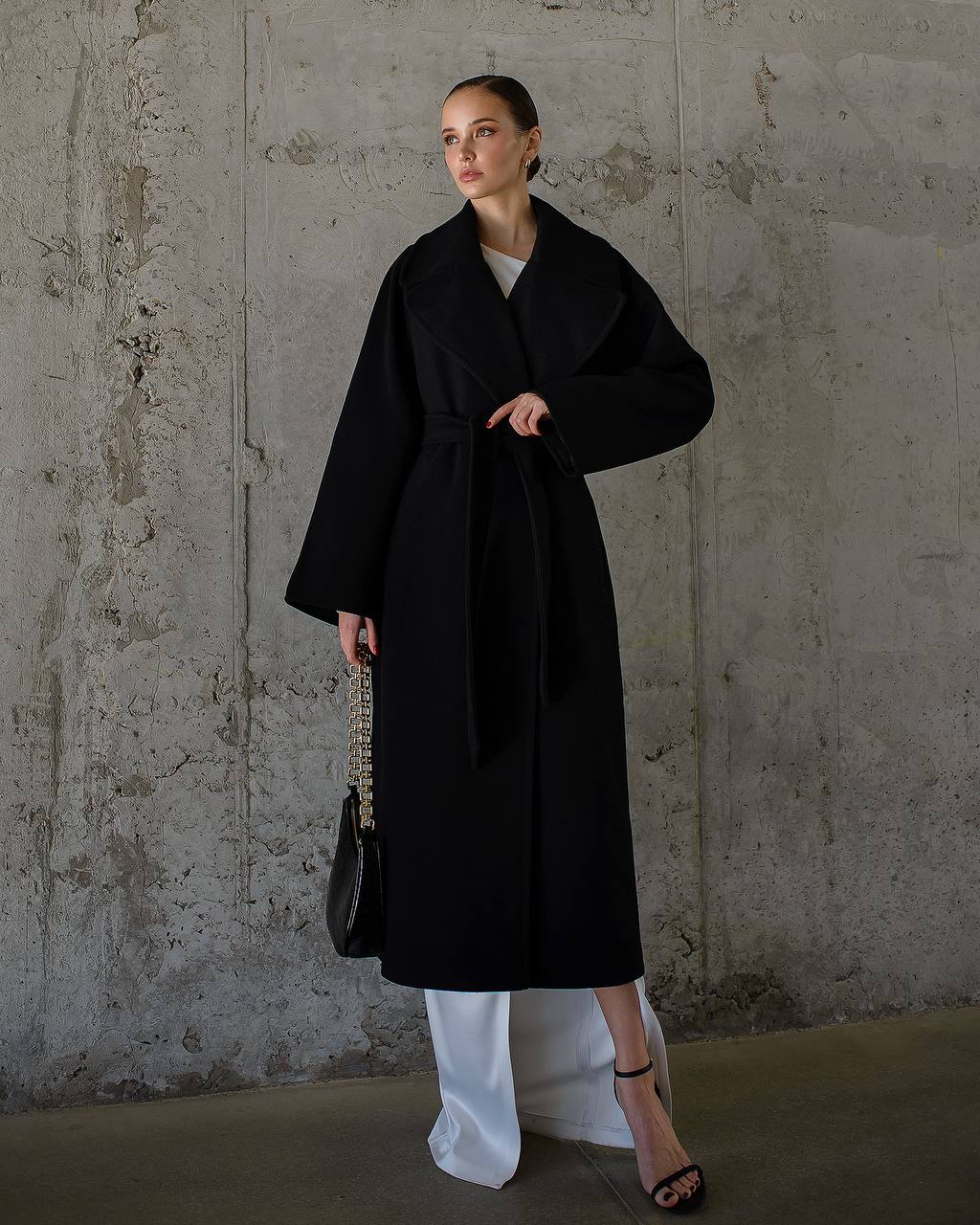 Woman wearing a black coat against a textured wall.
