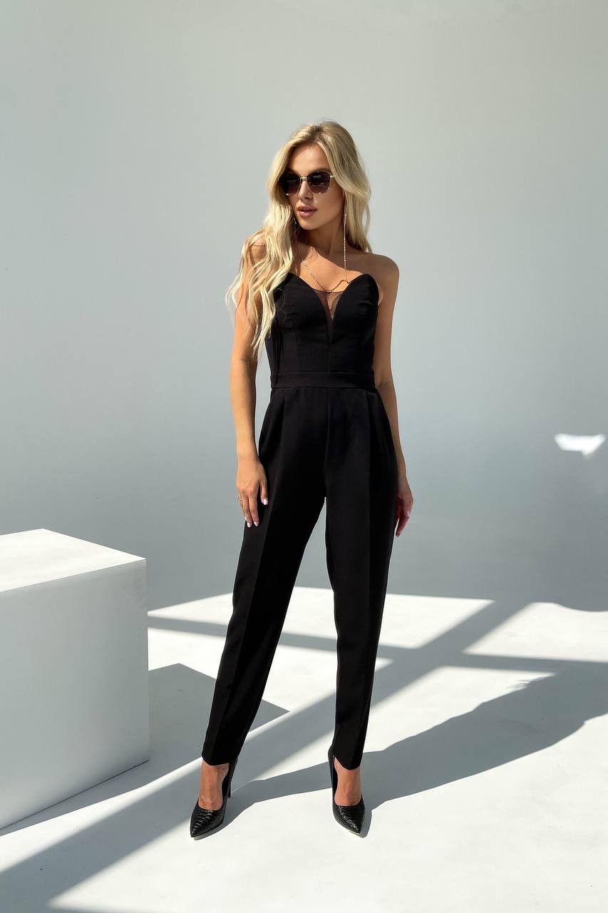 Woman wearing a black jumpsuit standing against a white background