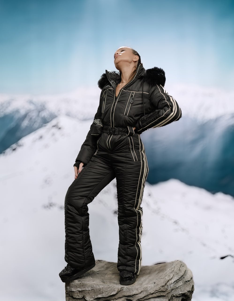 Person wearing a black winter suit with fur trim on a snowy mountain background