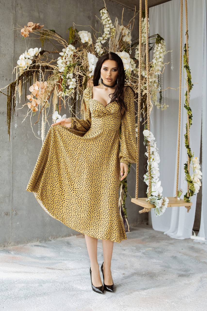Woman in a gold dress standing in a decorated room with flowers and hanging plants.
