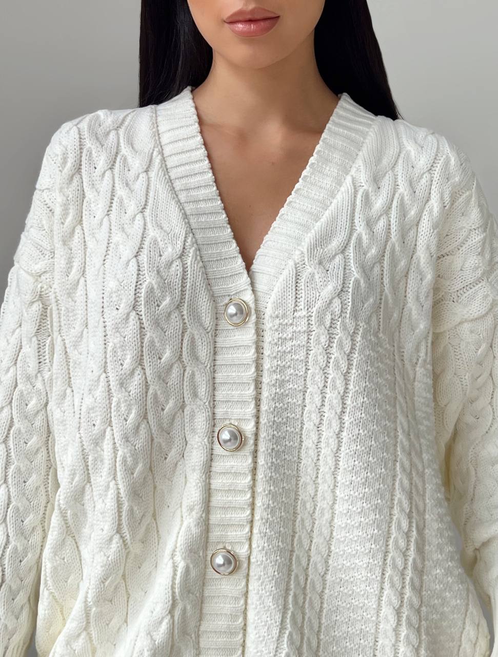 Close-up of a person wearing a white cable knit cardigan with pearl buttons.