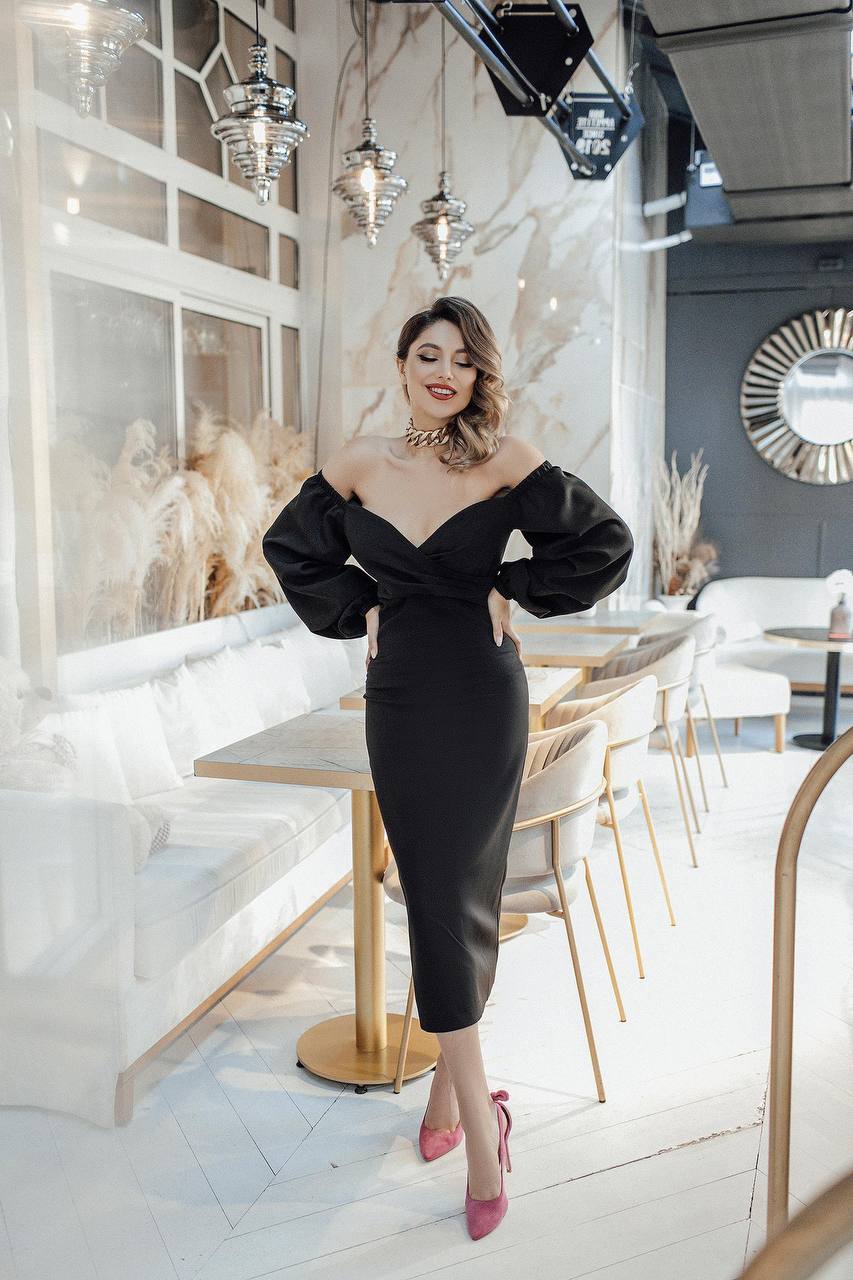 Woman in a black off-shoulder dress standing in an elegant interior setting.
