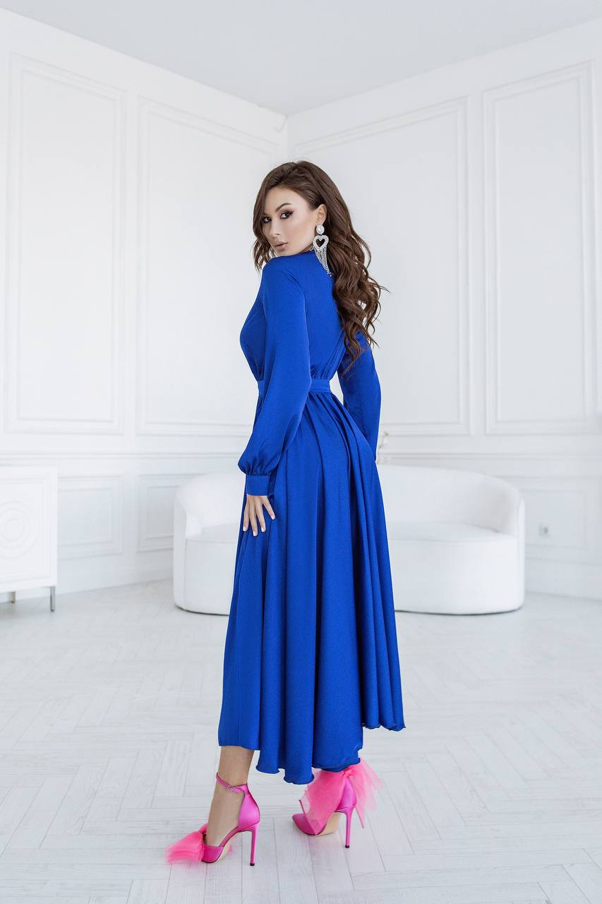 Woman in a blue dress with pink high heels standing in a white room.