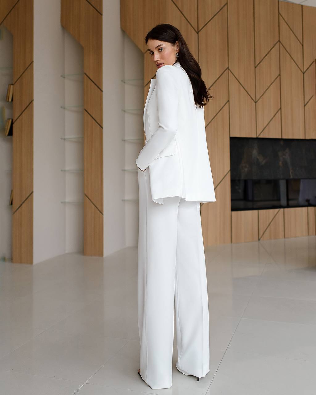 Woman in a white suit standing in a modern room with wooden walls.