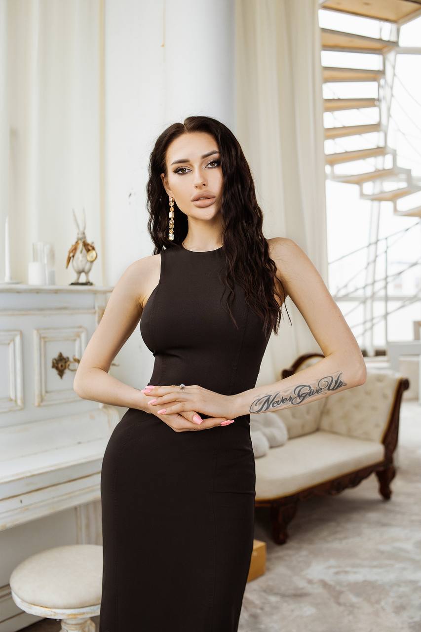 Woman in a black dress standing in an elegant room with a staircase.