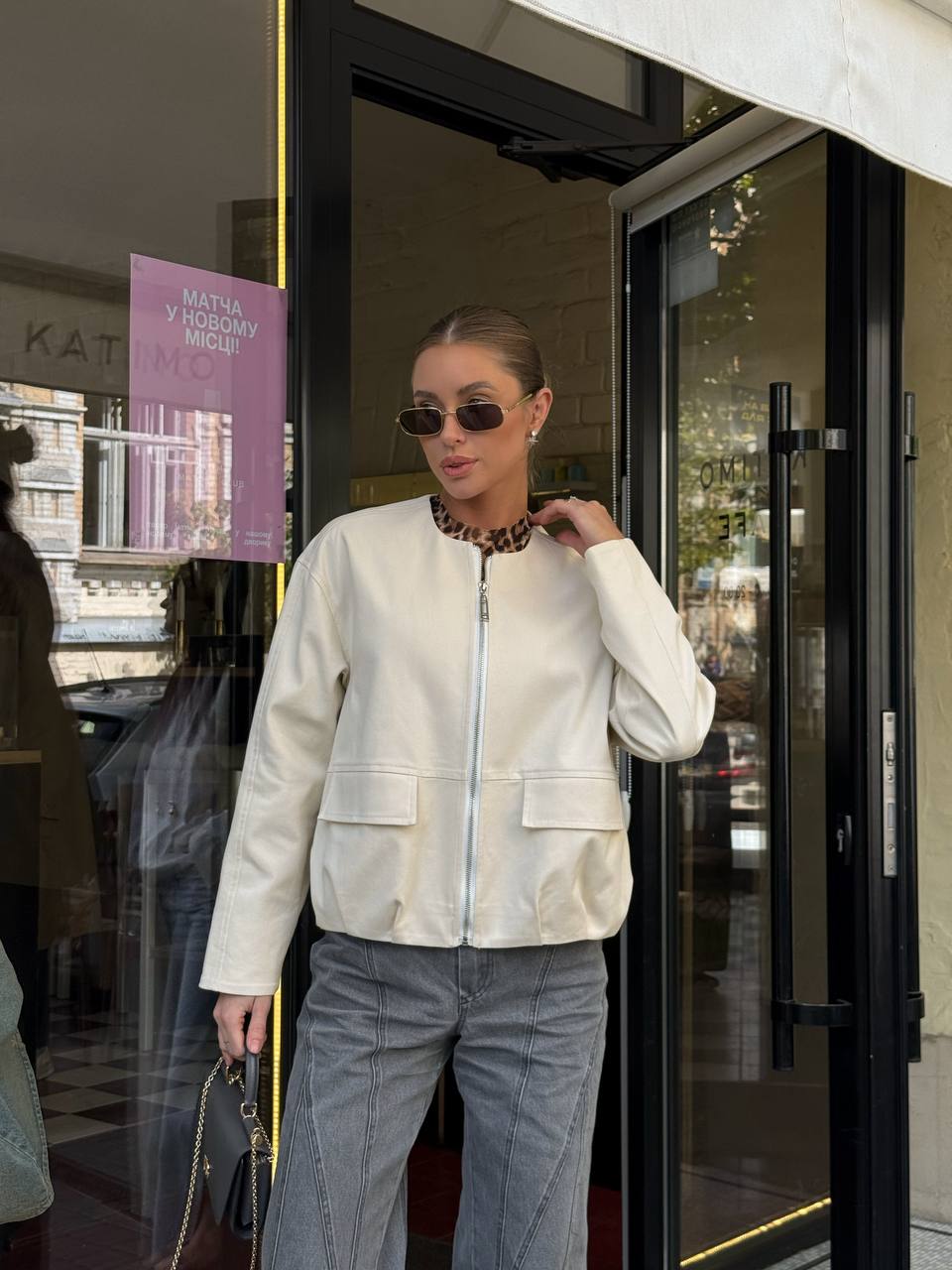 Woman in a white jacket and jeans standing outside a store with a blurred background