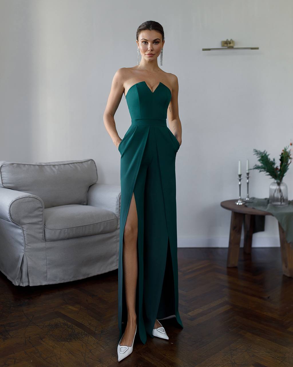 Woman in a strapless green evening gown standing in a room with a gray sofa and wooden table.