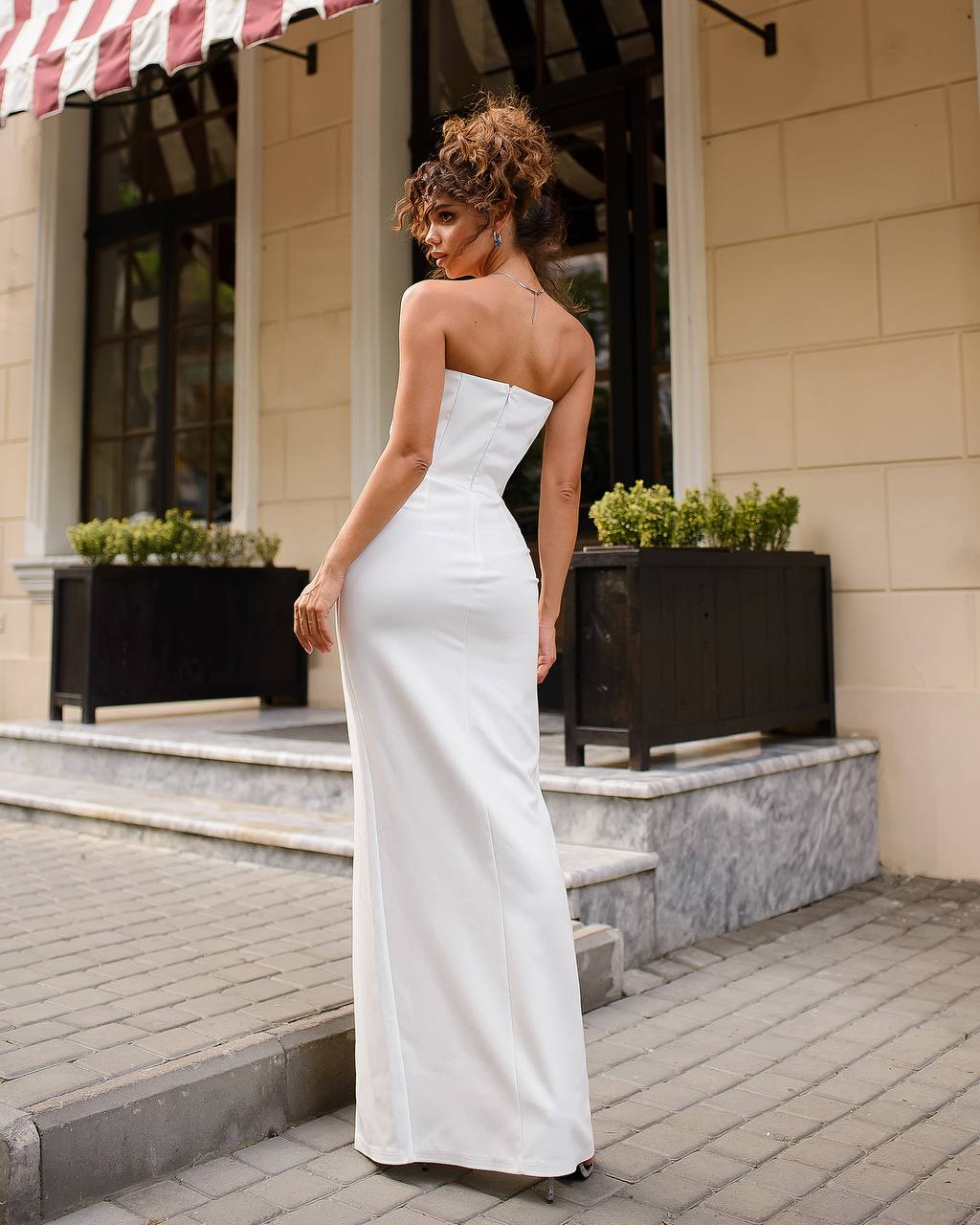 Woman in a white strapless gown standing on a sidewalk with a building in the background