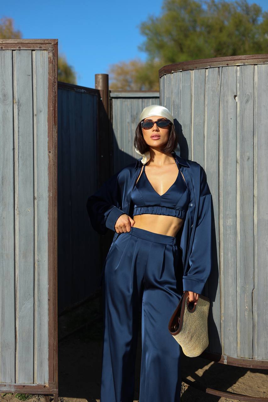 Woman in a blue outfit standing against a wooden fence with trees in the background