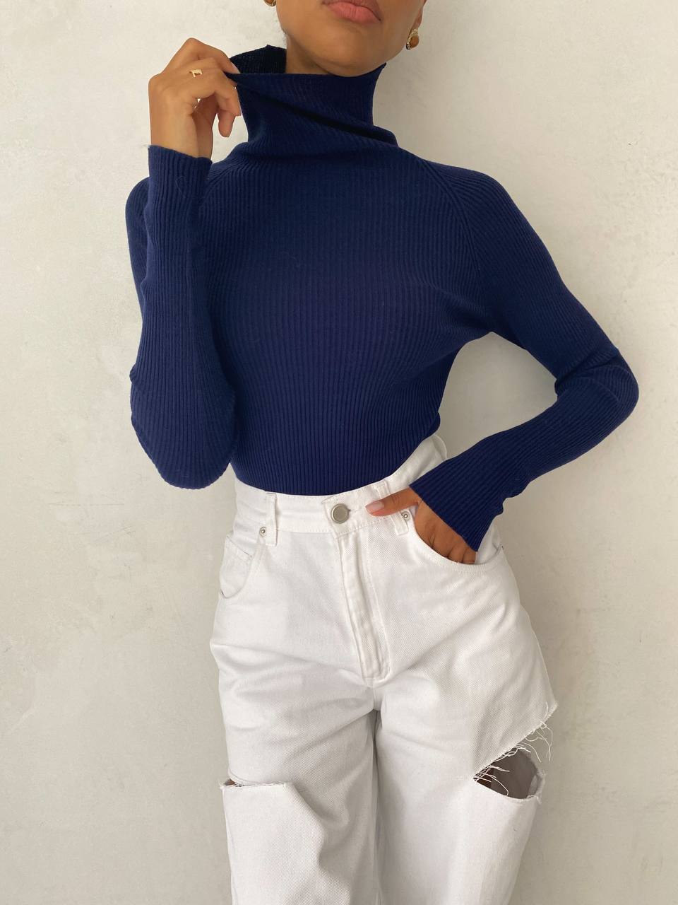 Person wearing a navy blue turtleneck sweater and white jeans against a plain background