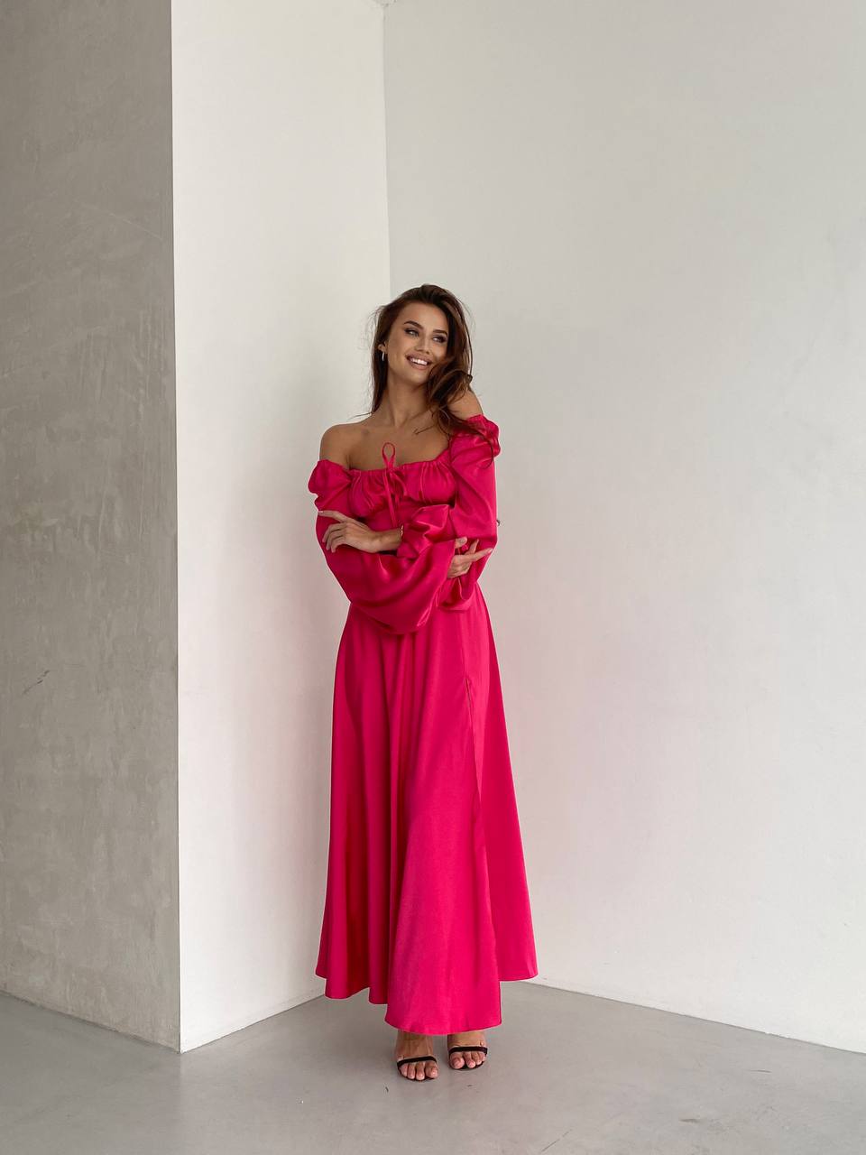 Woman wearing a bright pink off-shoulder dress against a plain white wall.