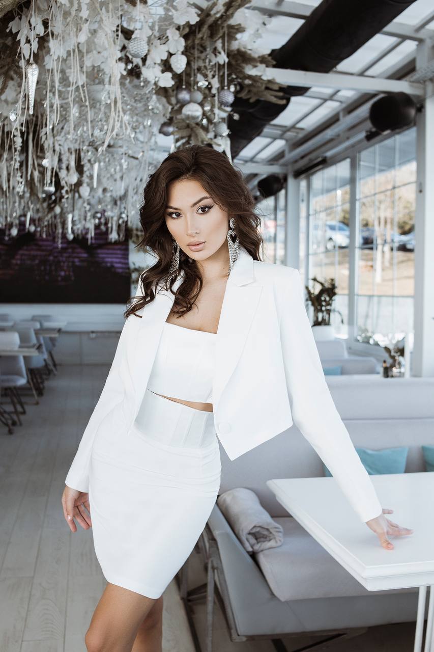 Woman in a white outfit standing in an elegant indoor setting with chandeliers.