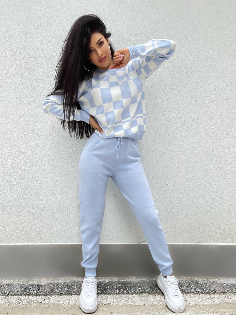 Woman wearing a checkered sweater and light blue pants against a plain background
