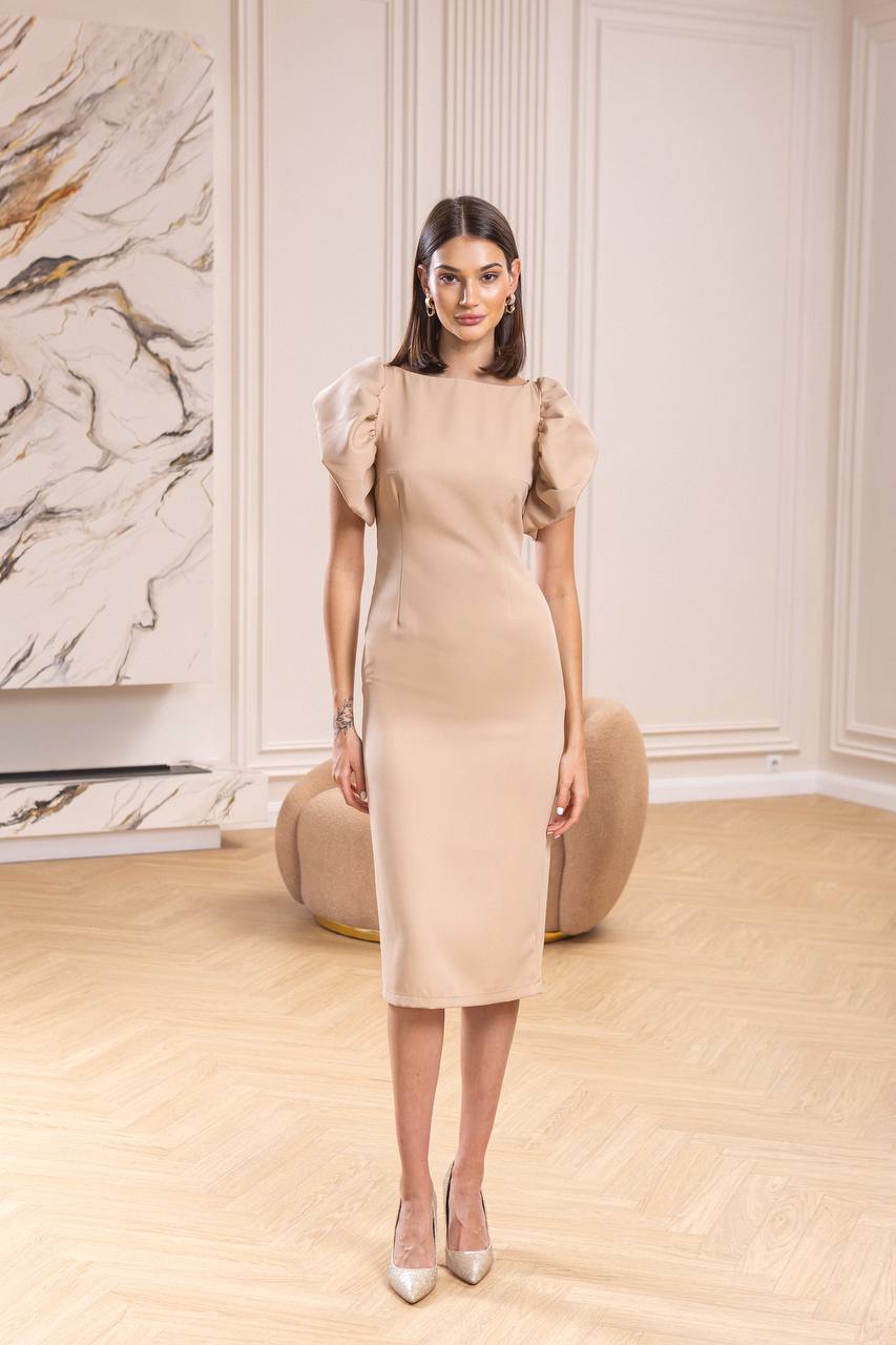 Woman wearing a beige dress with puffed sleeves in an elegant room.