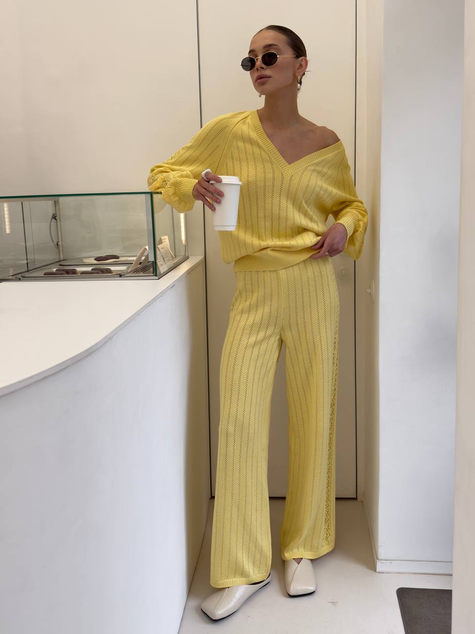 Woman in a yellow outfit holding a white cup in an indoor setting.