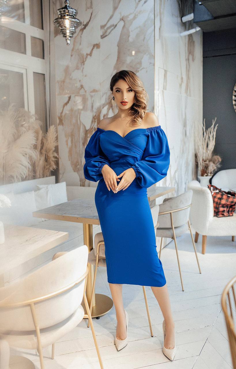 Woman in a blue off-shoulder dress standing in a modern interior setting.