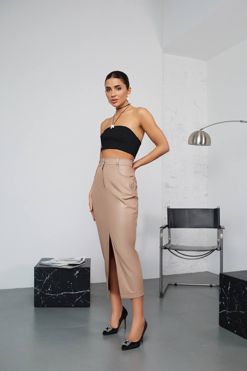 Woman in black top and beige skirt posing in a modern room.