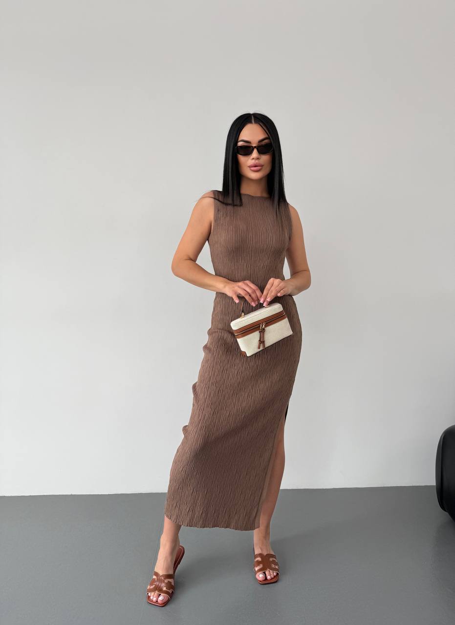 Woman wearing a brown dress holding a clutch against a plain background