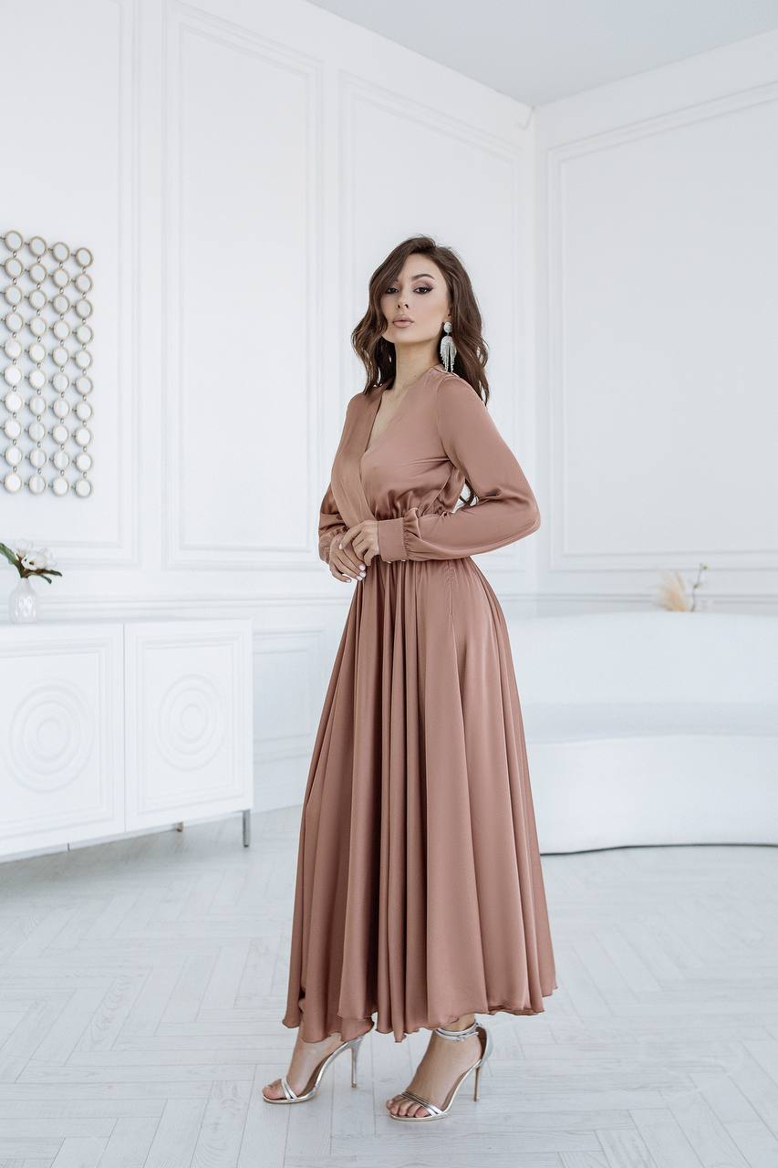 Woman wearing a long, light brown dress in a minimalistic room.