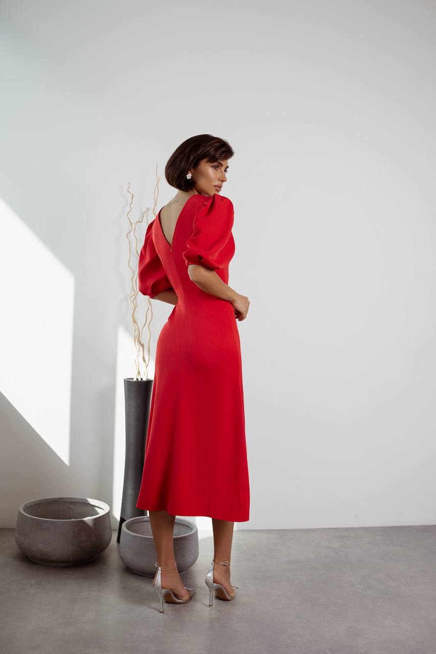 Woman in a red dress standing in a minimalistic room with white walls and gray floor.