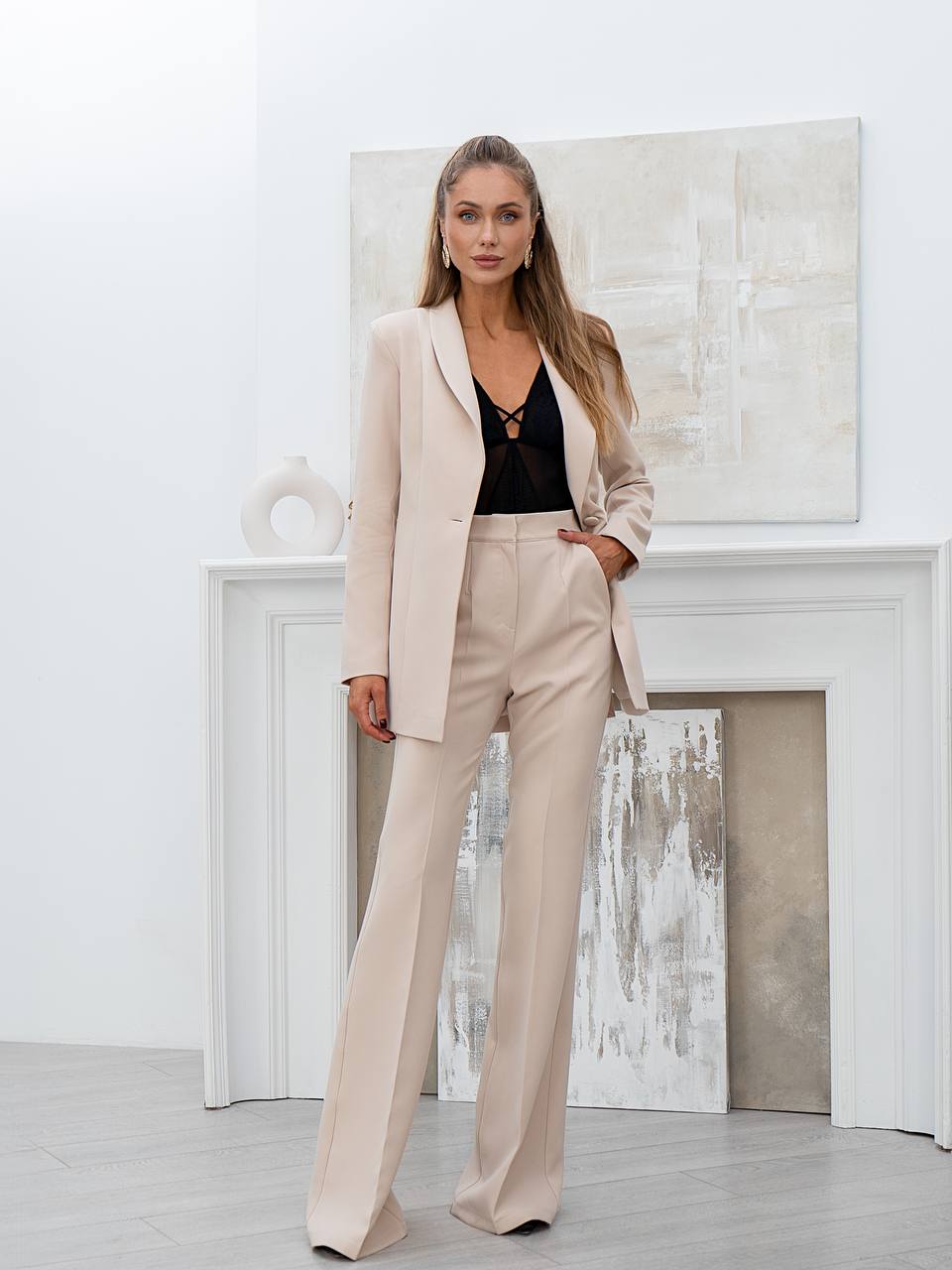 Woman in a beige suit standing in a modern interior setting with abstract art on the wall.