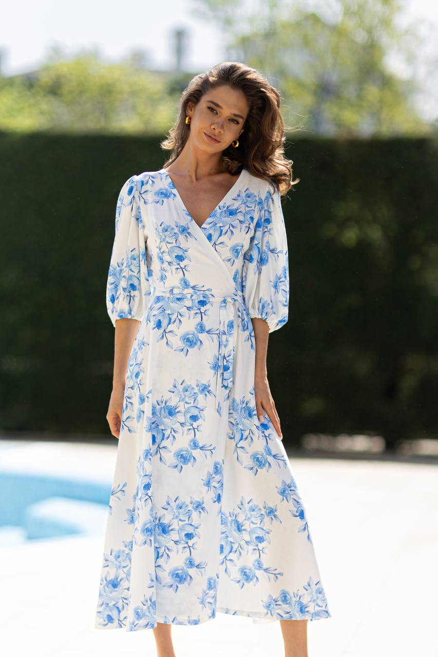 Woman wearing a white dress with blue floral patterns by a poolside.