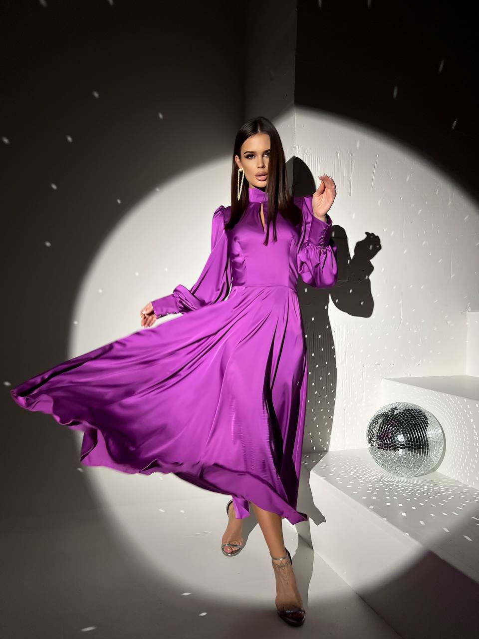 Woman in a purple dress standing in a spotlight with a disco ball in the background