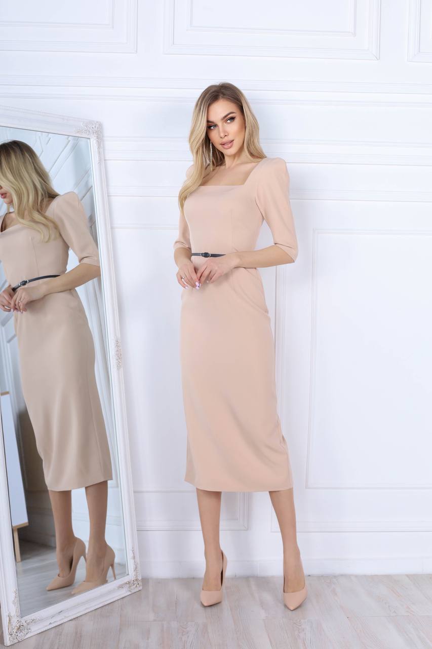 Woman wearing a beige dress standing in front of a mirror with a white wall background