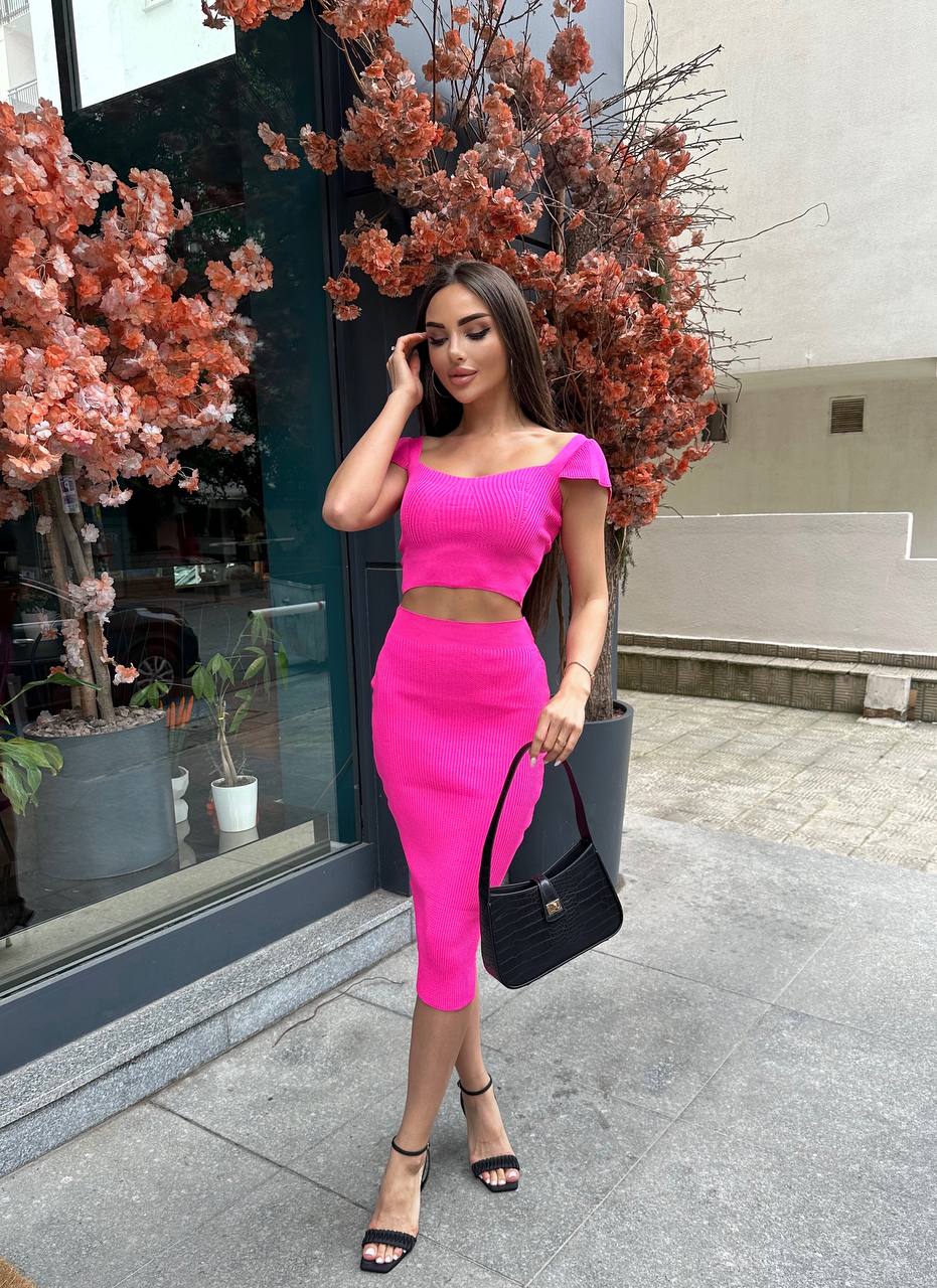 Woman in a bright pink outfit standing outdoors with decorative plants in the background