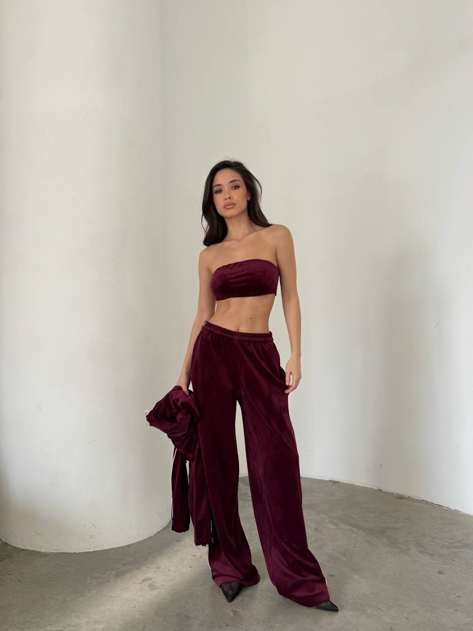 Woman wearing a burgundy strapless top and wide-leg pants against a plain background