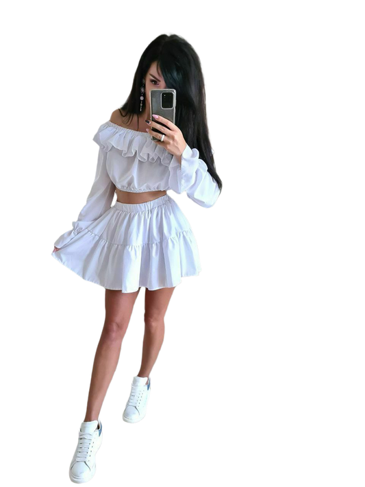 Woman taking a mirror selfie wearing a white outfit with ruffled details on a white background