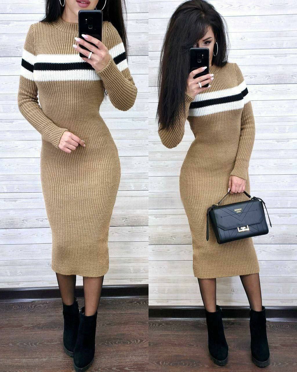 Woman wearing a beige ribbed dress with black and white stripes, holding a black handbag.