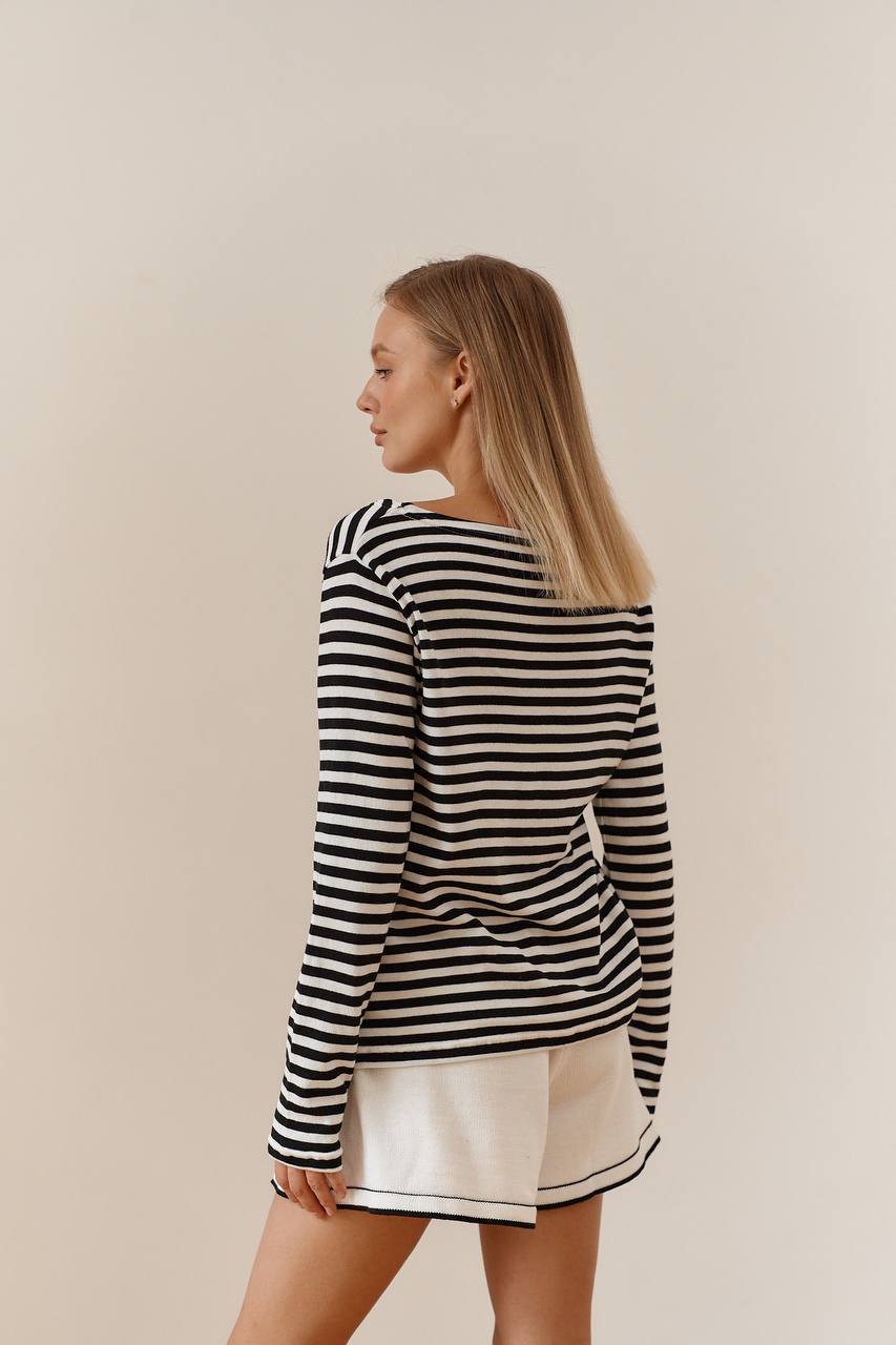 Woman wearing a black and white striped long-sleeve top and beige shorts on a beige background