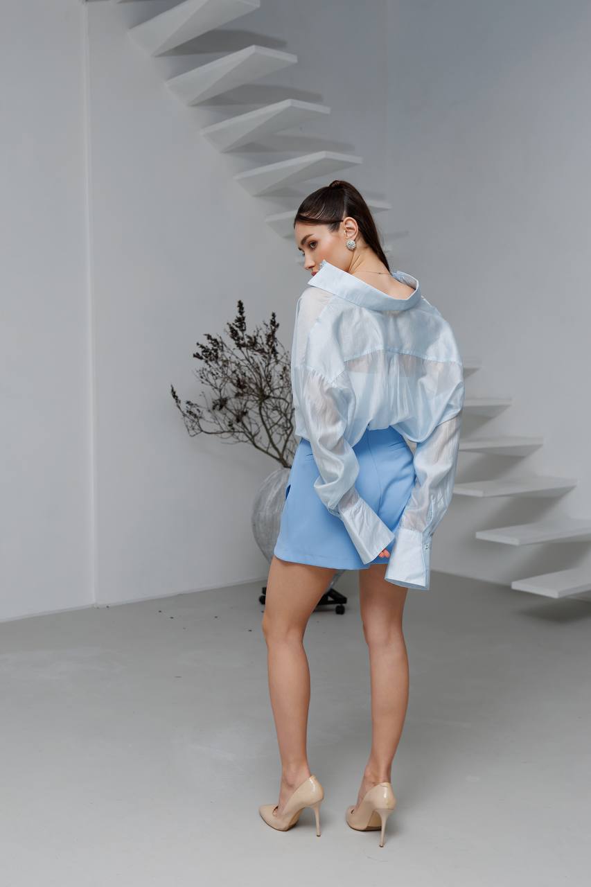 Woman wearing a light blue outfit with a sheer top in a minimalistic setting