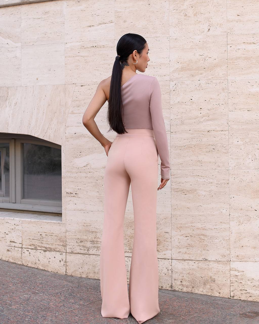 Woman in a pink outfit standing against a beige stone wall.