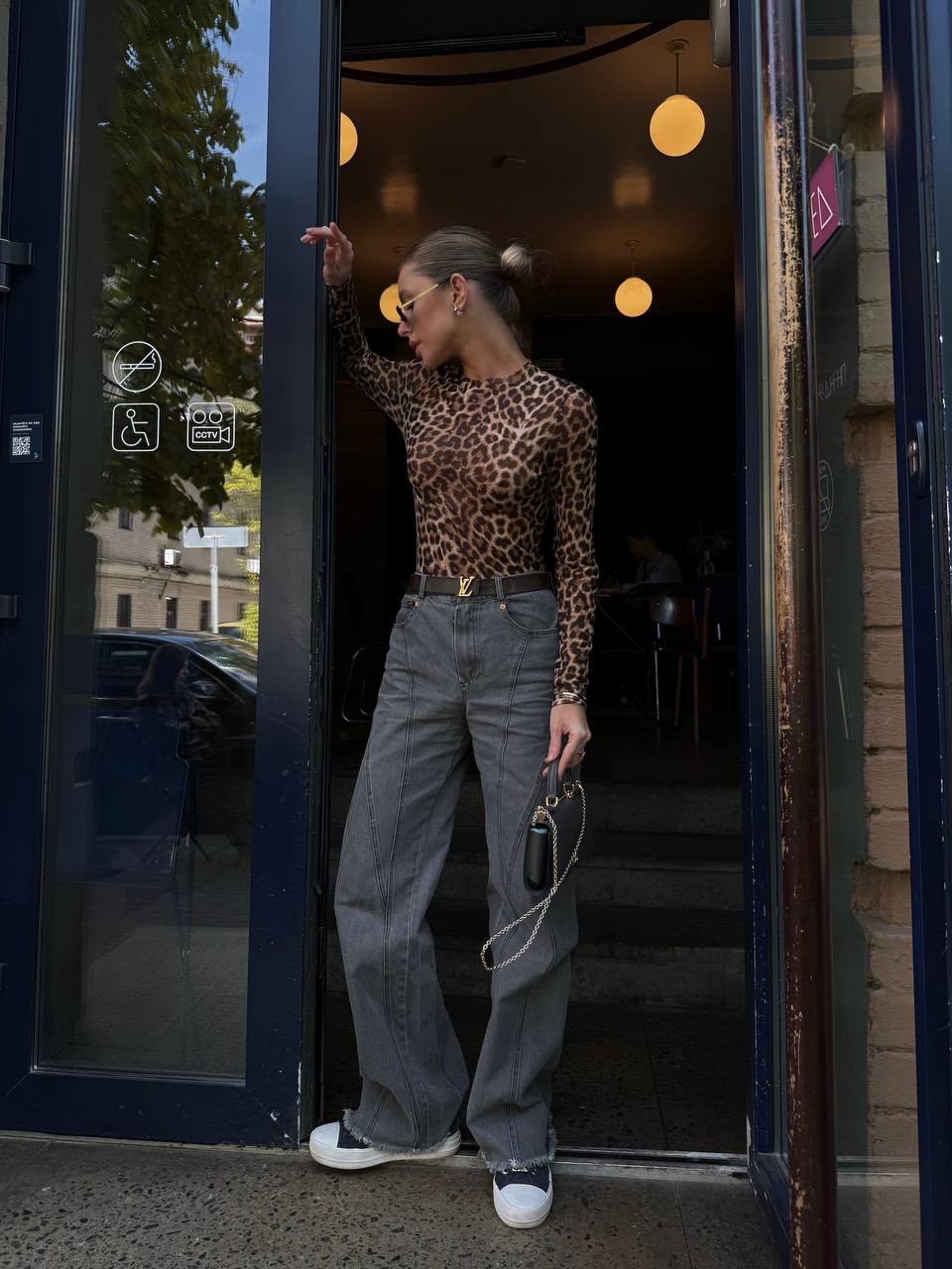 Person wearing a leopard print top and gray jeans exiting a building.