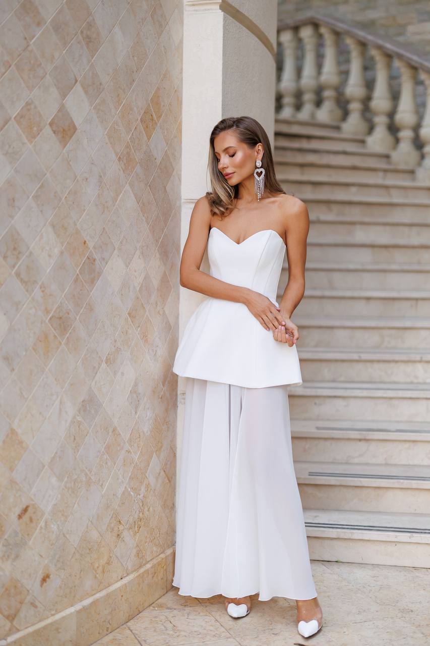 Woman in a white strapless top and wide-leg pants standing on stone steps.